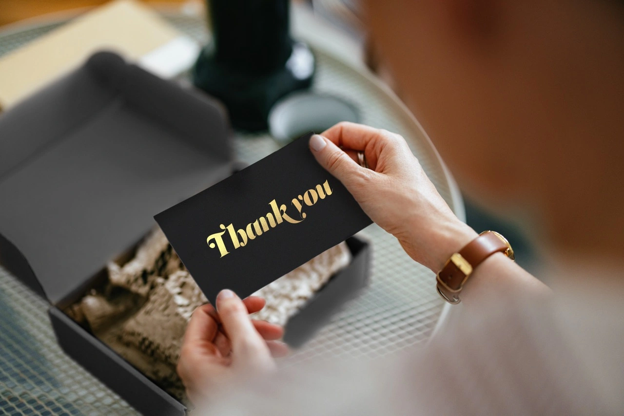 A woman takes out a black card with a golden writing thank you from a gift box